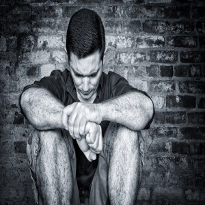 Sad young man sitting on the floor with a bricks background