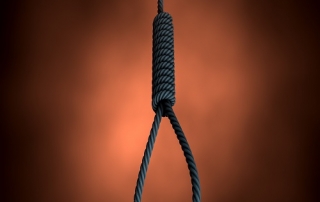 An eerie silhouetted view of a rope made into a hangmans noose on an orange backlit background