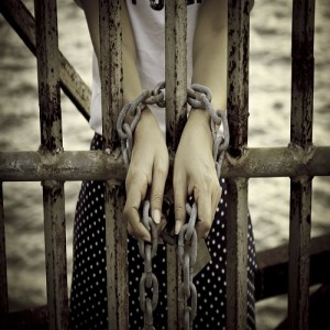 hands tied with rusty chain behind the bars
