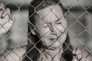 Portrait crying woman behind mesh wire fence, desperate, devastated, depressed, stressed facial expression, unhappy, closed eyes.